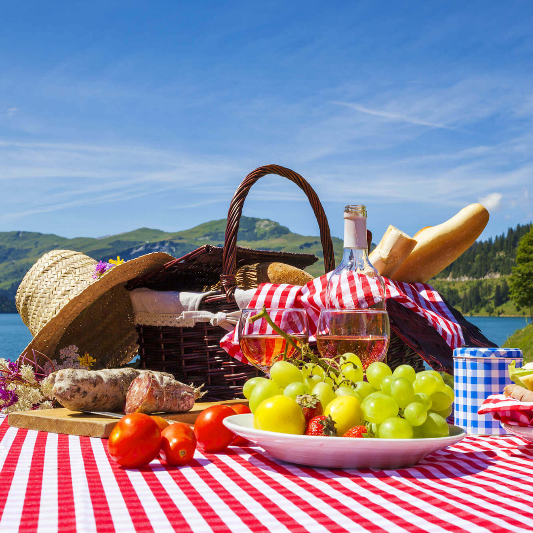 A picnic blanket, basket, and plate with food on it.