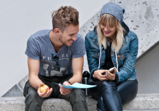 two students sitting down laughing and looking at a phone