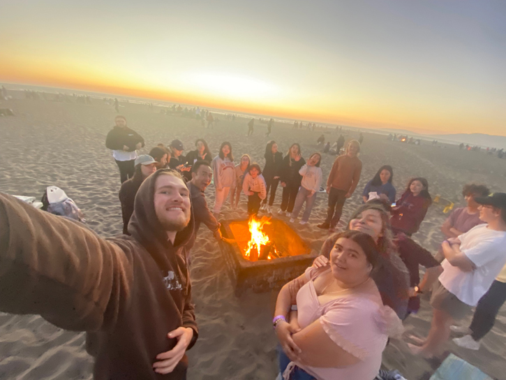 students posing for a photo on a beach with a fire