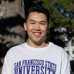 Averie has short black hair and is wearing stud earrings. He is wearing a white, long-sleeve SF State shirt.