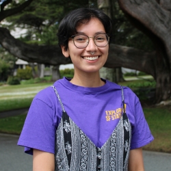 A girl with short dark brown hair smiling and wearing a purple shirt.