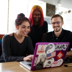 A group of 3 students around a laptop working on a project