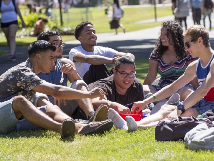 Students sitting together on the University quad, talking, and smiling. 