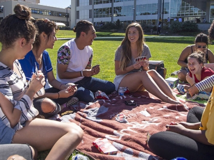 Group of students sitting on a blanket in the quad playing Uno